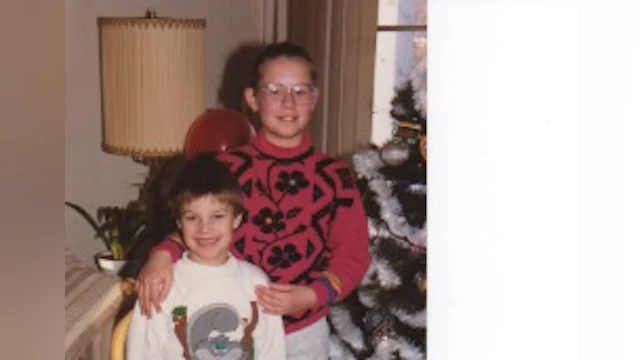 Two children smiling next to a Christmas tree.