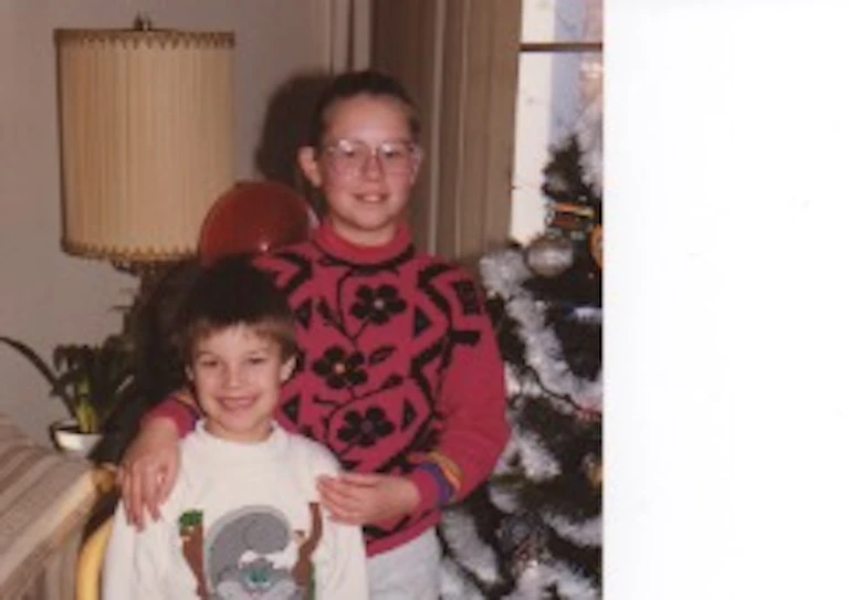 Two children smiling next to a Christmas tree.