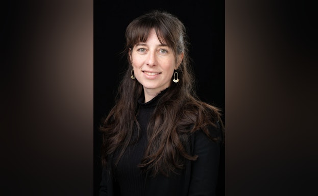 Maggie Sugg smiling against a black background.