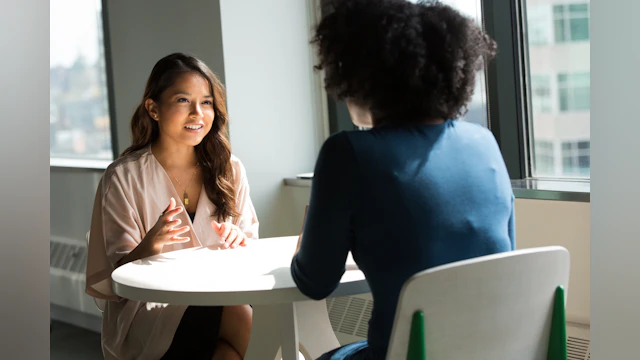 Two people sit at a table talking across from one another