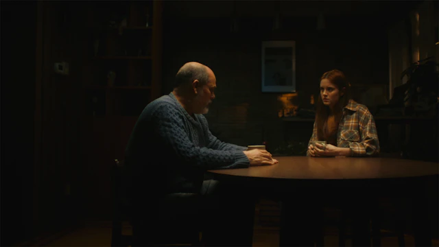 A dad and daughter sit at a table togther talking in a dark room
