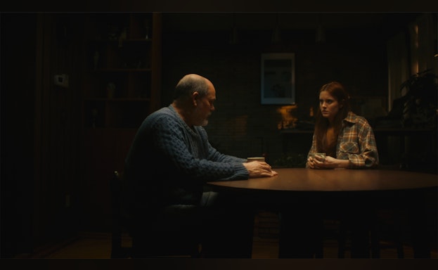 A dad and daughter sit at a table togther talking in a dark room