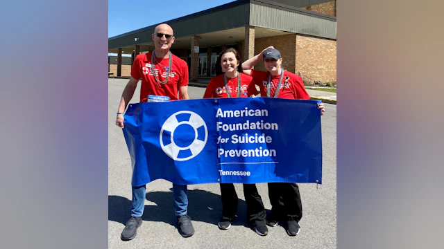 Three people holding a blue banner with the AFSP logo