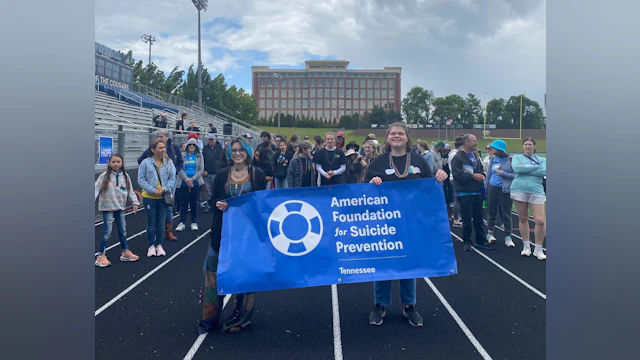 Two teenagers holding a blue banner with the AFSP logo