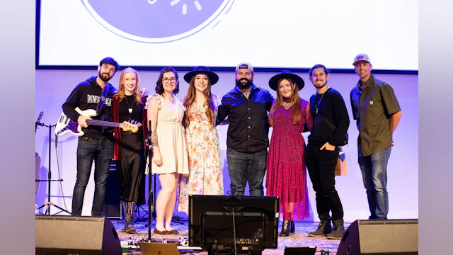 A group of eight people gather for a photo on stage