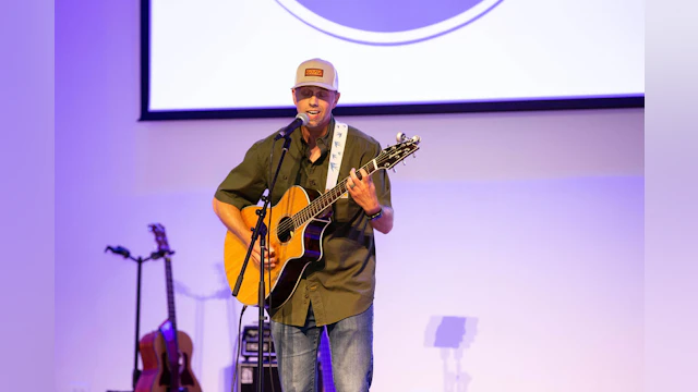 A man holds a guitar and sings on stage