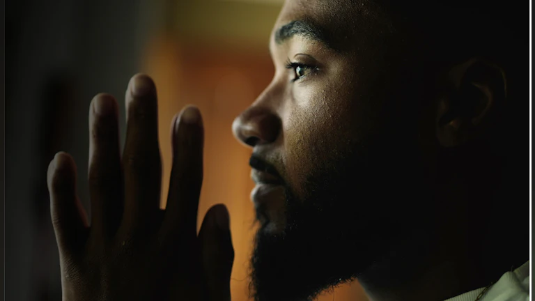 Side profile photo of person with beard looking ahead of them and raising hand