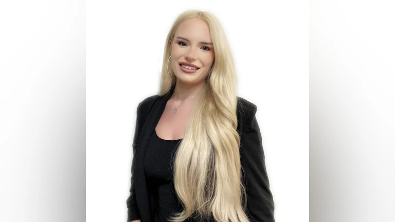 The author, Willow Danielle, smiling against a white backdrop. She is wearing a black top and black blazer.