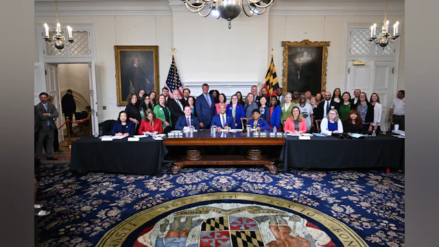 People stand in an ornate government room behind legislators signing bill