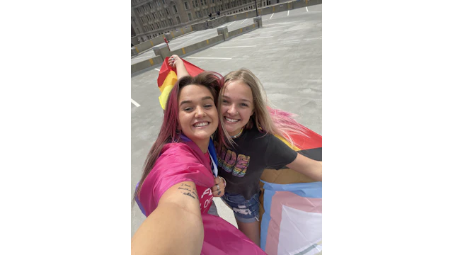 Taylor Ryan, pictured left, with the bisexual pride flag around her shoulders.