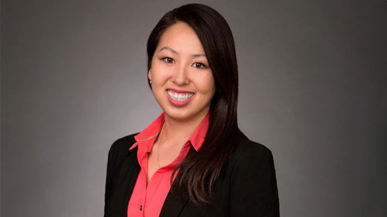 A headshot of the author, Darlene Tzou, smiling and wearing a salmon-pink shirt with a black blazer.