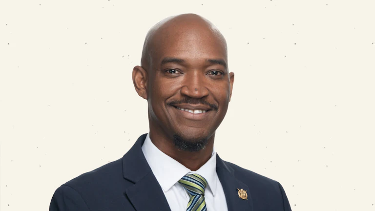 A headshot of the author, Keon Lewis, smiling and wearing a dark suit with a striped tie.
