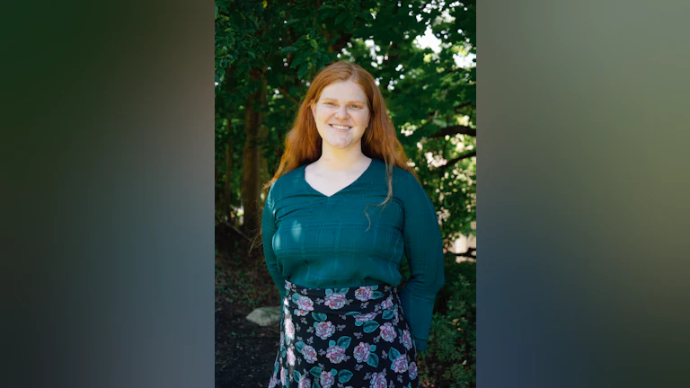 Anne Deubel standing outdoors, smiling, and wearing a floral skirt.