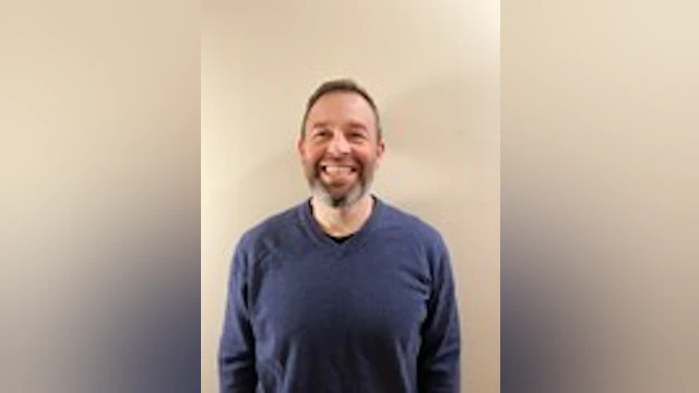 Dave Thompson smiling and wearing a long-sleeved, blue t-shirt.