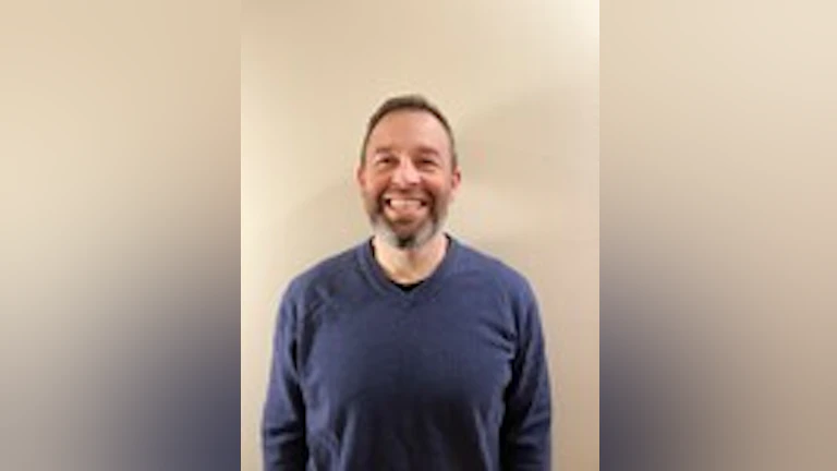 Dave Thompson smiling and wearing a long-sleeved, blue t-shirt.