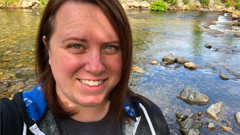 Angela Perry smiling outdoors in front of a clear body of water on a sunny day.