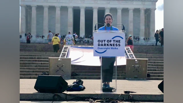 Marie standing at an outdoor podium, smiling and giving a speech at The Overnight.