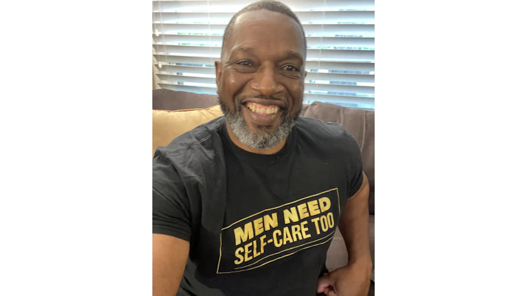 The author, Vic Armstrong, wearing a t-shirt that says "MEN NEED SELF-CARE TOO" in bright yellow block letters.