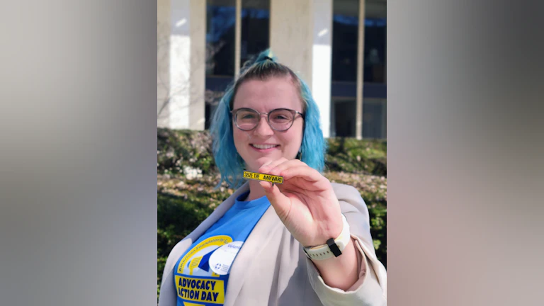 The author, Alaka'i Bene, smiling and wearing an Advocacy Action Day t-shirt while holding a "Seize the Awkward" pin.