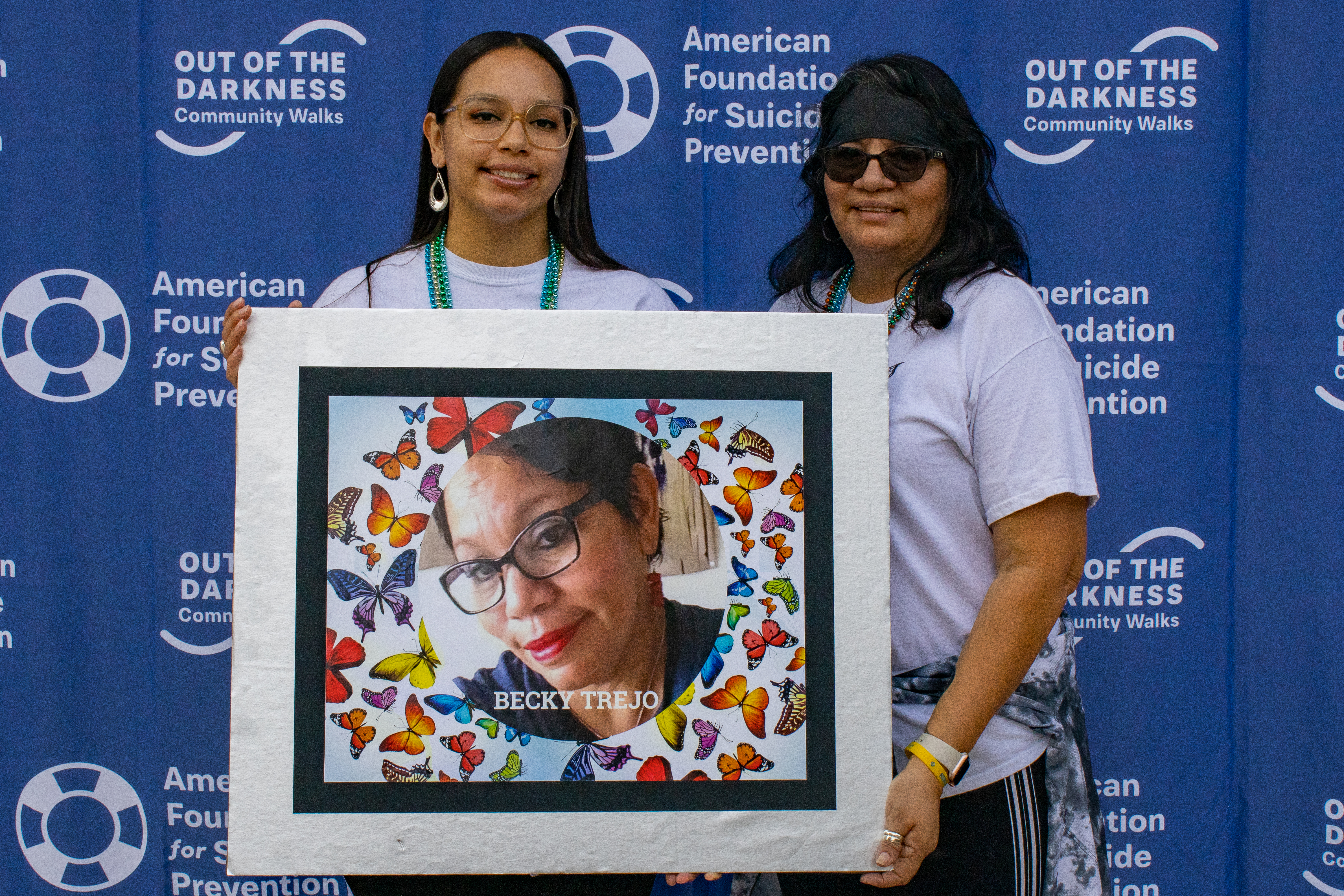 Two women holding a large photo of a woman smiling