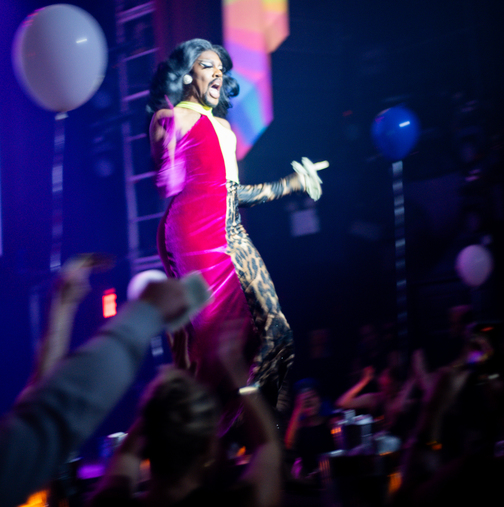 Drag performer wearing red dress and black wig in front of an audience