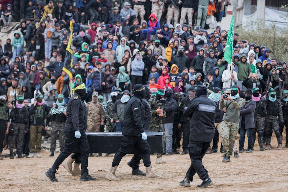 Hamas militants take pictures as fellow masked Palestinian fighters carry one of the coffins during the handover of the bodies of four Israeli hostages to the Red Cross in Khan Yunis in the southern Gaza on February 20, 2025. Hamas handed over on February 20 coffins believed to contain the bodies of four Israeli hostages, including those of the Bibas family who became symbols of the ordeal that has gripped Israel since the Gaza war began. The transfer of the bodies is the first by Hamas since its October 7, 2023 attack on Israel triggered the war, and is taking place under a fragile ceasefire that has seen living hostages exchanged for Palestinians held in Israeli prisons. (Photo by Abood Abusalama / Middle East Images / Middle East Images via AFP) (Photo by ABOOD ABUSALAMA/Middle East Images/AFP via Getty Images)