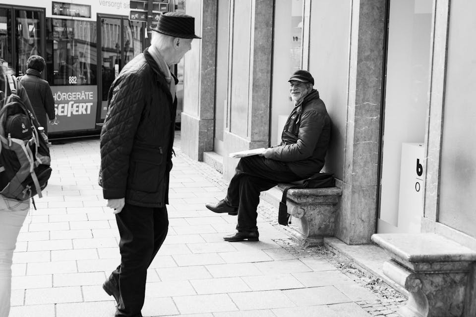 Augsburg, Germany – April 12, 2019: Two men exchange heartfelt smiles as one walks past the other who is sitting on a chair