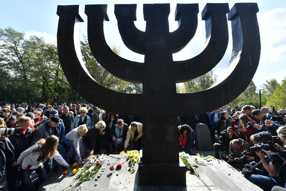 People lay symbolic stones and flowers at Minorah Monument at the Babyn Yar (Babi Yar) Holocaust Memorial in Kiev, on September 29, 2019, during a mourning ceremony marking the 78th anniversary of the beginning of mass execution of Jews in September 1941. – The Babi Yar (Babyn Yar) ravine in Kiev, was the location where Nazis shot dead several tens of thousands of Jews between 1941-1944. (Photo by Sergei SUPINSKY / AFP) (Photo by SERGEI SUPINSKY/AFP via Getty Images)