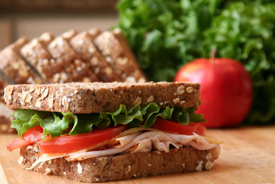 Healthy sandwich made with whole grain bread, lettuce, tomato, cheese, and roasted turkey slices.