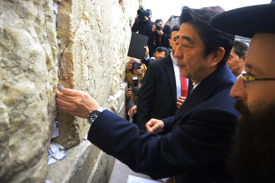 *Japanese Prime Minister Shinzo Abe places a note between stones of the Western Wall.* AP Photo/Mahmoud Illean. Abe-in-Israel-Main