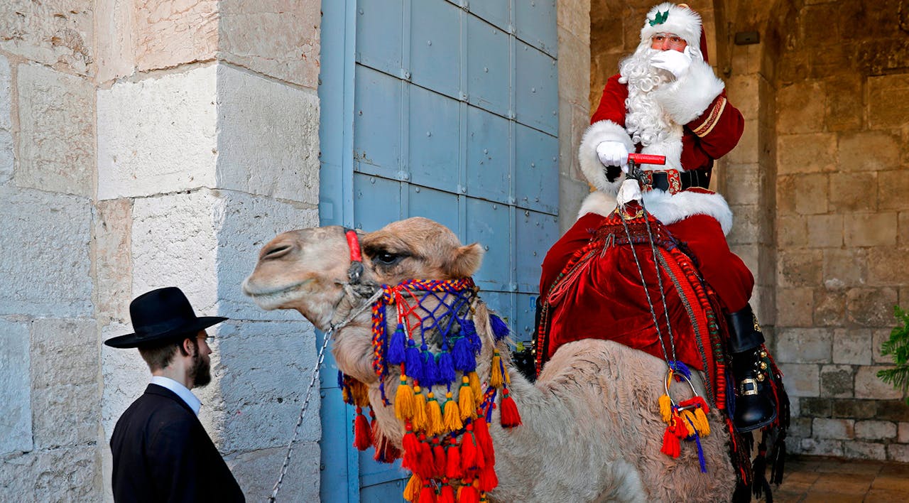 A man dressed up as Santa Claus gestures as he rides a camel before an ultra-Orthodox Jewish man in Jerusalem's Old City on December 19, 2019. *AHMAD GHARABLI/AFP via Getty Images.* McClay Main