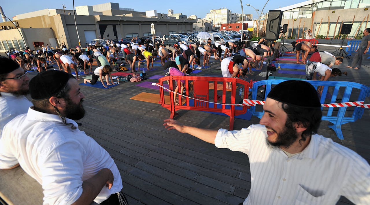 *Orthodox Israeli Jewish men watch as other Israelis gather in Tel Aviv for a mass outdoor yoga session to mark the longest day of the year on June 21, 2010*. YEHUDA RAIZNER/AFP via Getty Images. Wecker Yoga Main