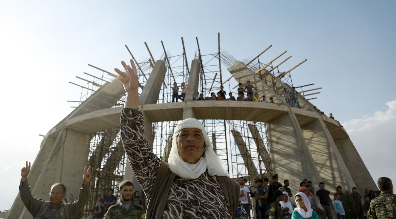 *A Syrian Kurdish woman flashes a victory sign during the June 24, 2016 funeral of fighters who died in an attack against Islamic State forces. In the background, a martyrs memorial is under construction.* DELIL SOULEIMAN/AFP/Getty Images. Haivry-Main