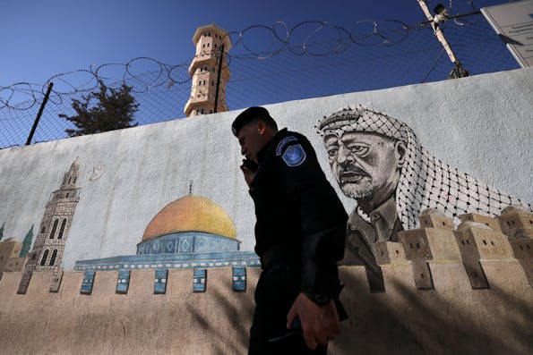 A Palestinian Authority policeman walks outside a police station adorned with a painting depicting late Palestinian leader Yasser Arafat, in the West Bank city of Hebron, on November 11, 2024, during the 20th anniversary of Arafat’s death, amid increased violence in Israeli-occupied Palestinian territory as the war between Israel and the Hamas movement continues in the Gaza Strip. (Photo by HAZEM BADER / AFP) (Photo by HAZEM BADER/AFP via Getty Images)
