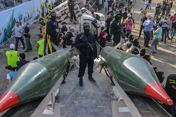 A fighter from the Saraya al-Quds Brigades, the armed wing of the Palestinian Islamic Jihad movement, stands between two rockets during a parade on the streets of Gaza City. *Mahmoud Issa/SOPA Images/LightRocket via Getty Images*. Gaza Missiles