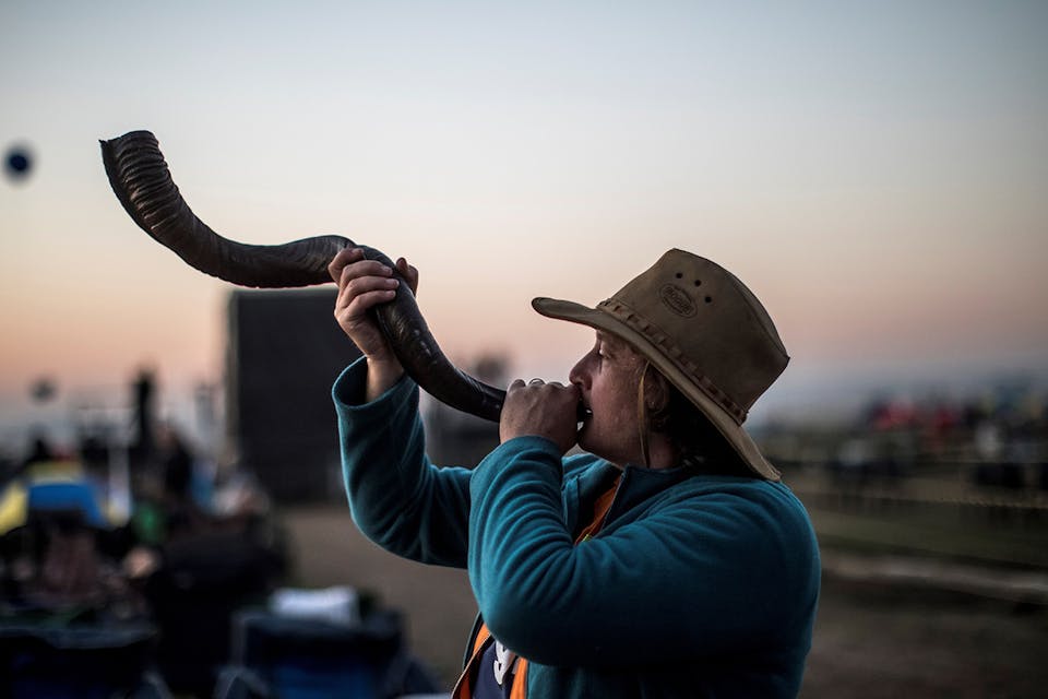 A follower of South African Christian revival evangelist Angus Buchan blows a shofar at an informal airfield outside Pretoria on October 27, 2018. *MARCO LONGARI/AFP via Getty Images.* McClay Last Word