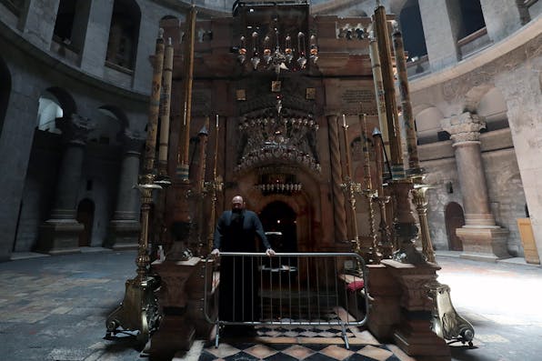 A Greek Orthodox monk stands behind a barricade at the entrance of the Edicule in the Church of the Holy Sepulchre, on May 26, 2020. *GALI TIBBON/AFP via Getty Images.* Levenson McClay Main