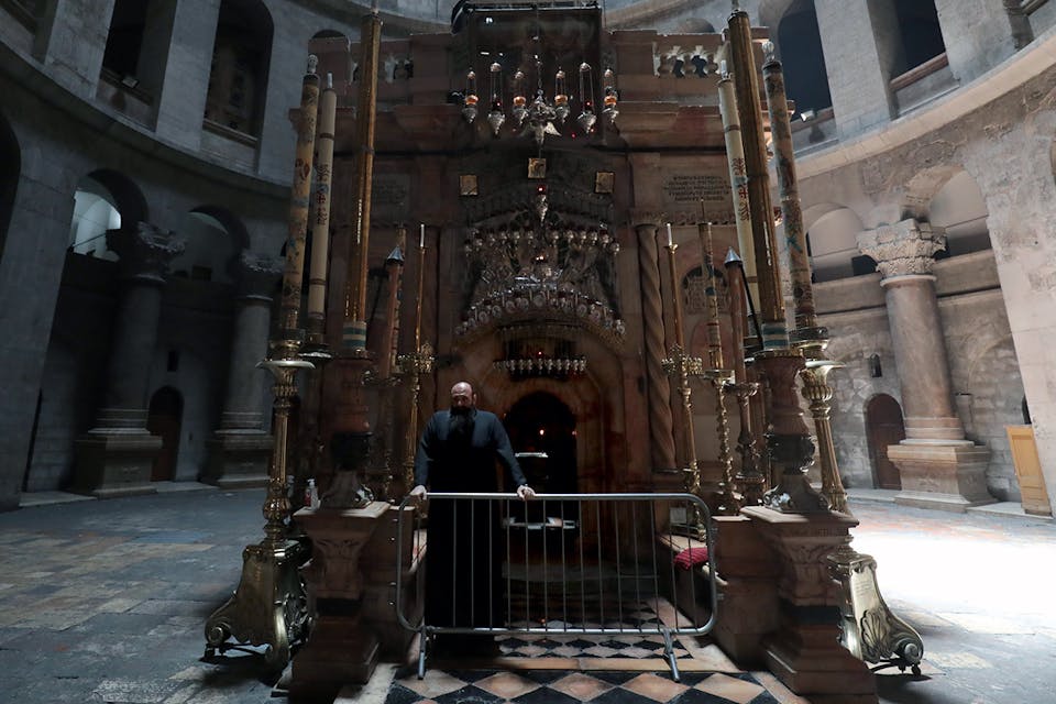 A Greek Orthodox monk stands behind a barricade at the entrance of the Edicule in the Church of the Holy Sepulchre, on May 26, 2020. *GALI TIBBON/AFP via Getty Images.* Levenson McClay Main