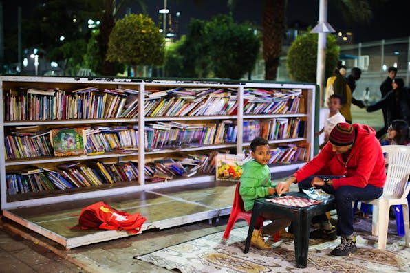 *A child and a man sit together at an outdoor book garden in Tel Aviv, December 9, 2015.* Esther Rubyan/Flash90. Horn