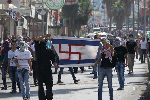 *Palestinian protesters hold up a makeshift Israeli flag, with a swastika replacing the Star of David, during a demonstration in the West Bank city of Hebron on October 16, 2015*. HAZEM BADER/AFP/Getty Images. Taheri-Main