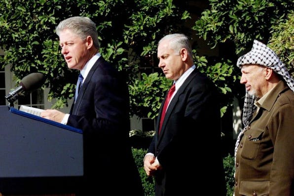 Bill Clinton, Benjamin Netanyahu, and Yasir Arafat outside the White House on October 15, 1998, before negotiating the Wye River memorandum. *PAUL RICHARDS/AFP via Getty Images.* WASHINGTON, DC – OCTOBER 15: US President Bill Clinton (L) speaks at a Middle East Peace Accords ceremony in the Rose Garden of the White House in Washington, DC as Israeli Prime Minister Benjamin Netanyahu (C) and Palestinian leader Yasser Arafat (R) look on15 October. All three leaders are scheduled to attend a tri-lateral summit on Middle East peace at the 1,000 acre secluded Wye River Plantation conference center located on the Eastern shore of Maryland. (ELECTRONIC IMAGE) (Photo credit should read PAUL RICHARDS/AFP via Getty Images)