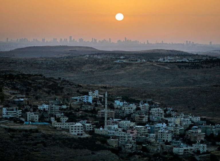 The Tel Aviv skyline, as seen from Na’ale, just northwest of Ramallah, June 17, 2020. *Menahem Kahana/AFP via Getty Images.* TOPSHOT – A picture taken from the Israeli settlement of Naale in the occupied West Bank northwest of the Palestinian city of Ramallah shows the skyline of the Israeli coastal city of Tel Aviv on June 17, 2020. – The government of Israeli Prime Minister Benjamin Netanyahu has said it could begin the process to annex Jewish settlements in the West Bank as well as the strategic Jordan Valley from July 1. The plan — endorsed by Washington — would see the creation of a Palestinian state, but on reduced territory, and without Palestinians’ core demand of a capital in east Jerusalem. (Photo by MENAHEM KAHANA / AFP) (Photo by MENAHEM KAHANA/AFP via Getty Images)