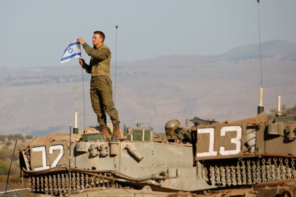 An Israeli soldier places a flag atop a tank during a military drill near the border with Lebanon in the Upper Galilee, October 26, 2023. *Jalaa Marey/AFP via Getty Images.* TOPSHOT – An Israeli soldier places a national flag atop a Merkava tank during in a military drill near the border with Lebanon in the upper Galilee region of northern Israel on October 26, 2023, amid the ongoing battles between Israel and the Palestinian group Hamas in the Gaza Strip. (Photo by Jalaa MAREY / AFP) (Photo by JALAA MAREY/AFP via Getty Images)
