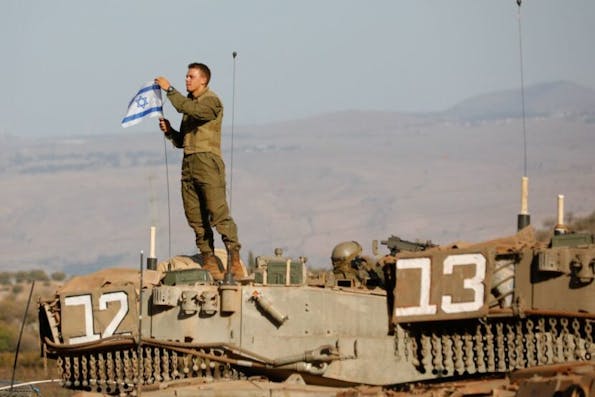 TOPSHOT – An Israeli soldier places a national flag atop a Merkava tank during in a military drill near the border with Lebanon in the upper Galilee region of northern Israel on October 26, 2023, amid the ongoing battles between Israel and the Palestinian group Hamas in the Gaza Strip. (Photo by Jalaa MAREY / AFP) (Photo by JALAA MAREY/AFP via Getty Images)
