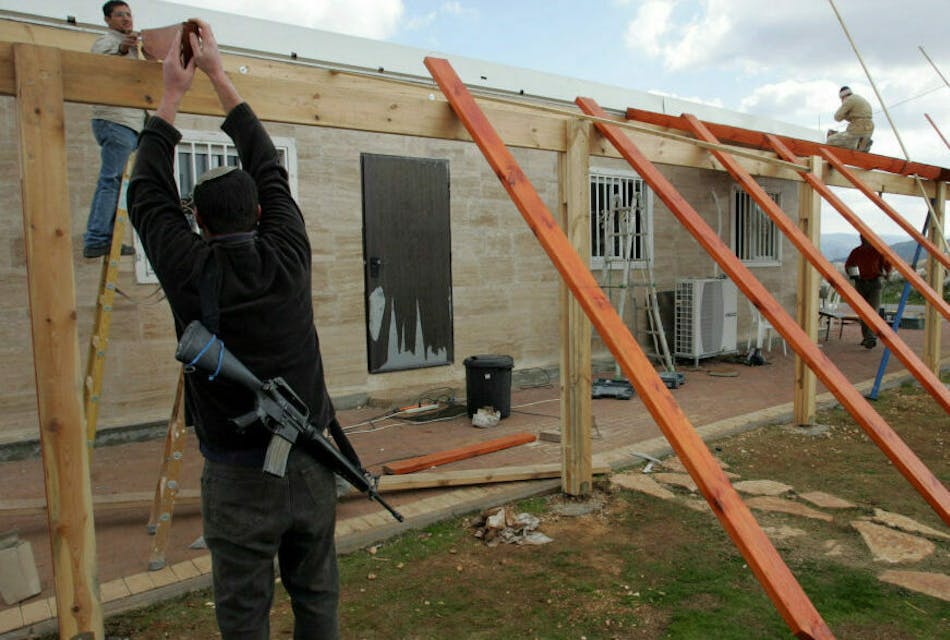 An armed Jewish settler works with a Palestinian construction worker on a synagogue in the unauthorized West Bank outpost of Bruchin, 08 January 2008. The Israeli government is seeking a court ban on the publication of a key report on settlements, a peace group said on today, just days before US President George W. Bush begins a landmark visit.
AFP PHOTO/JACK GUEZ (Photo by JACK GUEZ / AFP) (Photo by JACK GUEZ/AFP via Getty Images)
