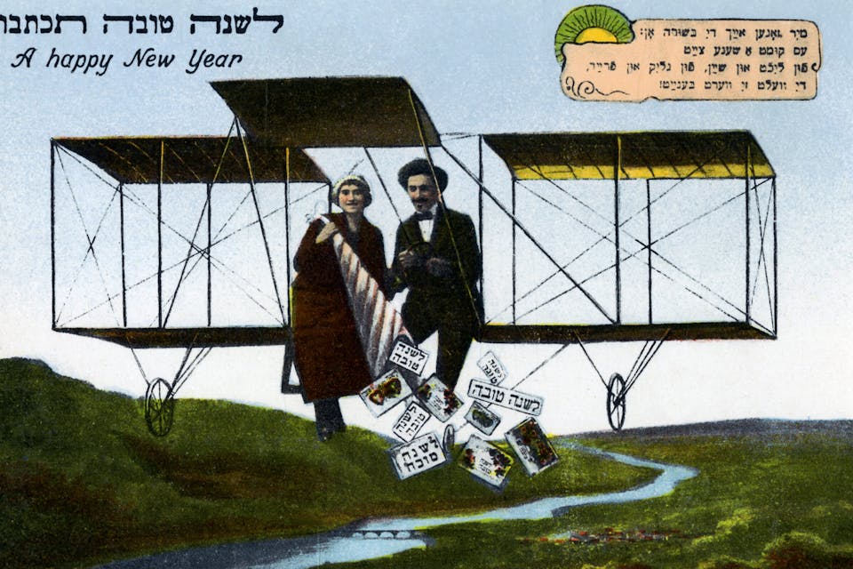A postcard featuring a couple flying on an early airplane throwing holiday greetings to the ground below, with New Year's greetings in Hebrew and English. *Pierce Archive LLC/Buyenlarge via Getty Images*. A Jewish postcard featuring a couple flying on an early airplane throwing holiday greetings to the ground below. Text in Hebrew and English wishing one a Happy Jewish New Year. Artist unknown (Photo by Pierce Archive LLC/Buyenlarge via Getty Images)