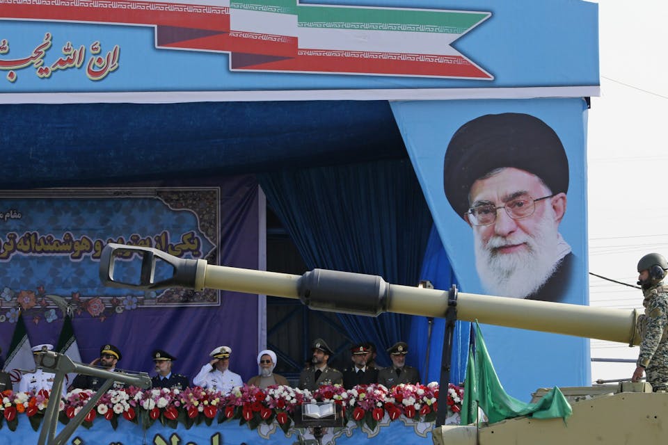 During a parade in Tehran celebrating Iran's annual army day, a tank rolls past a portrait of Iran's Supreme Leader Ayatollah Ali Khamenei on April 18, 2018. *Photo by ATTA KENARE/AFP via Getty Images.* An Iranian army tank rolls past the tribune decorated with a portrait of Iran’s Supreme Leader Ayatollah Ali Khamenei during a parade on the occasion of the country’s annual army day on April 18, 2018 in Tehran. – President Hassan Rouhani said during the parade that Iran “does not intend any aggression” against its neighbours but will continue to produce all the weapons it needs for its defence. (Photo by ATTA KENARE / AFP) (Photo by ATTA KENARE/AFP via Getty Images)