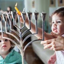 Young girl lights the Hanukkah menorah with help from adult