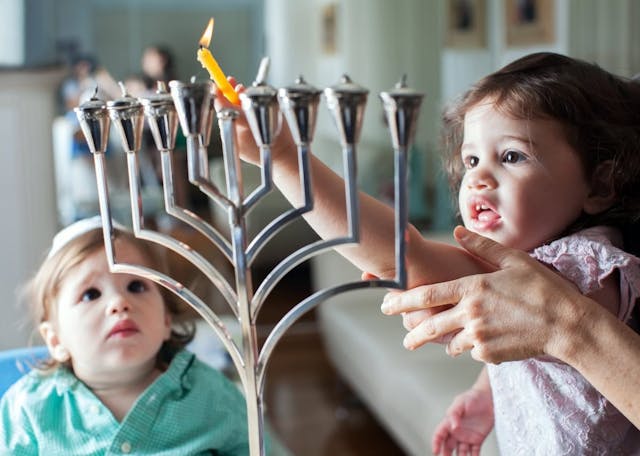 Young girl lights the Hanukkah menorah with help from adult