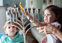 Young girl lights the Hanukkah menorah with help from adult